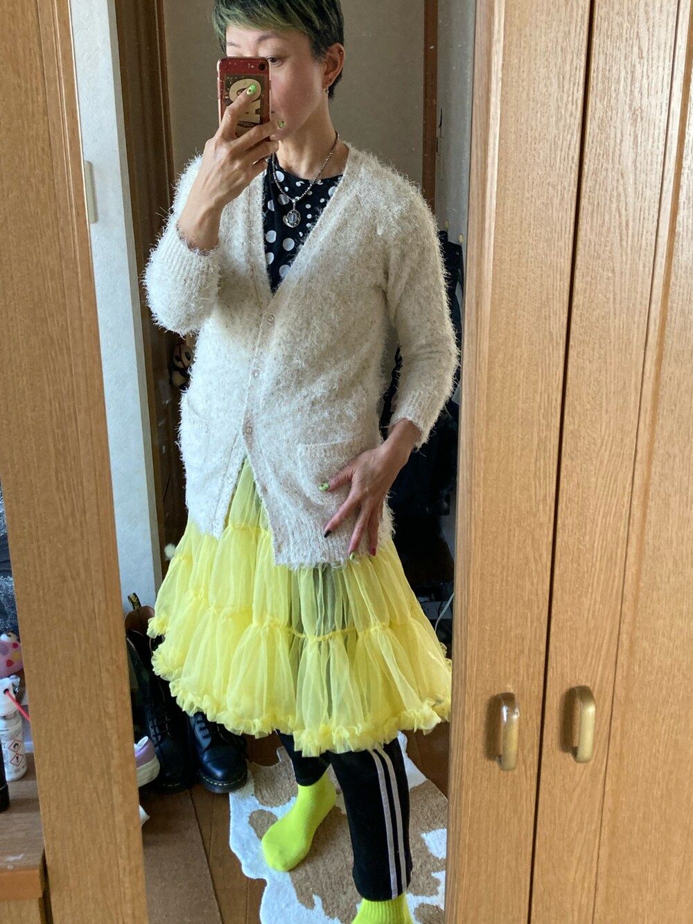 ブラック系のジャージ、ホワイト系のカーディガン/ボレロ、イエロー系のスカートを着用したレディースの冬コーディネートの2枚目の写真