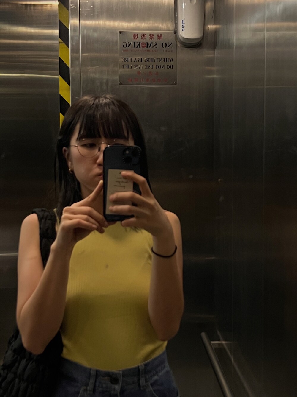 イエロー系のタンクトップ、ブラック系のバッグ、ブルー系のデニムパンツを着用したレディースの夏コーディネートの2枚目の写真