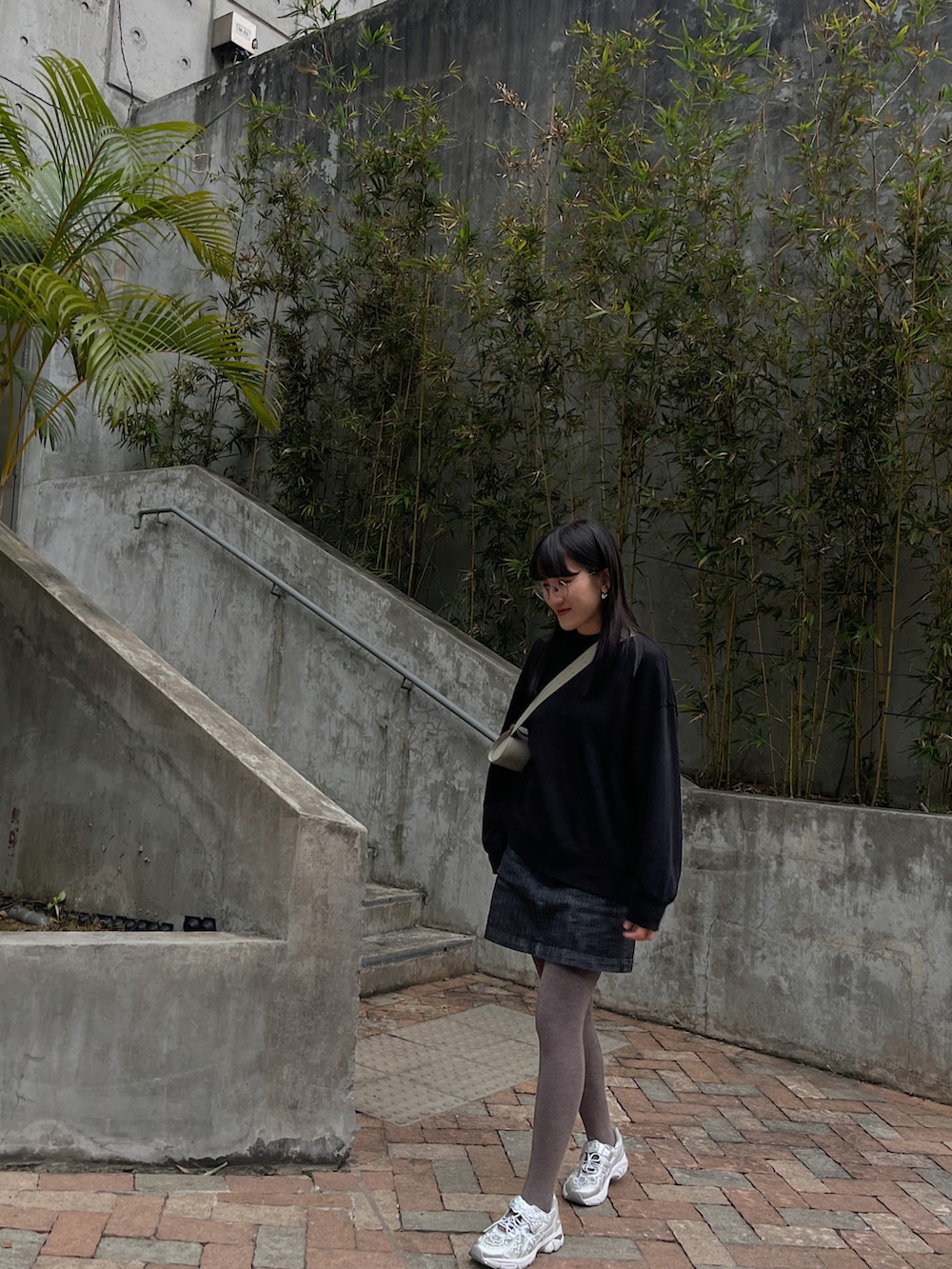 グリーン系のバッグ、ブラック系のトップス、シルバー系のスニーカーを着用したレディースの冬コーディネートの2枚目の写真