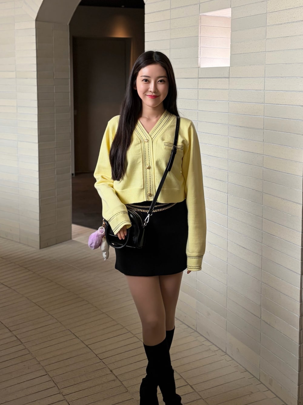 ブラック系のブーツ、イエロー系のカーディガン/ボレロ、ブラック系のスカートを着用したレディースの春コーディネートの2枚目の写真