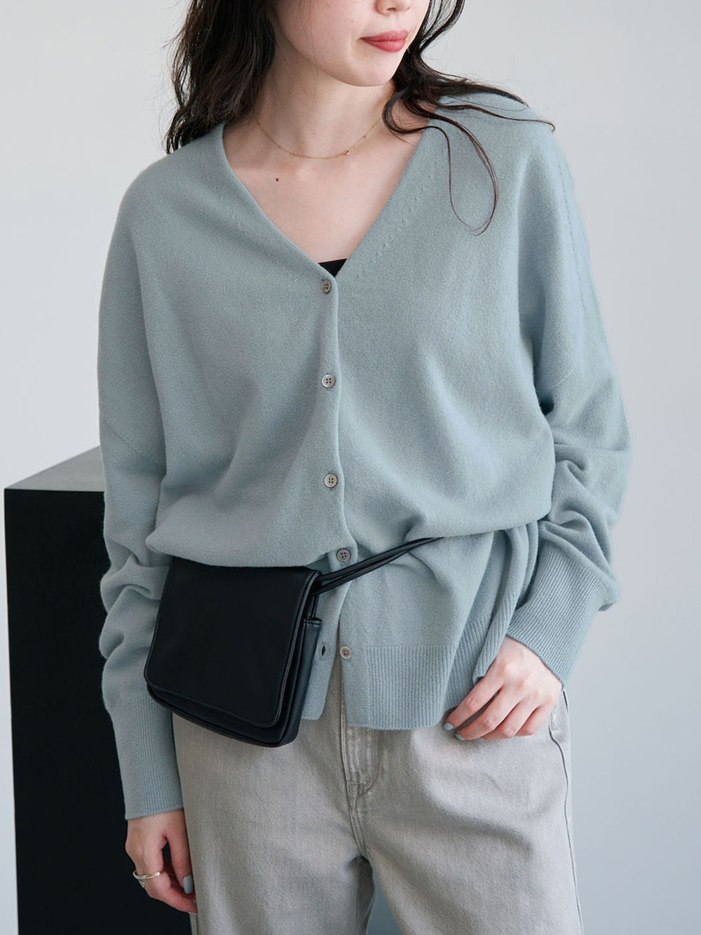グレー系のデニムパンツ、ブルー系のカーディガン/ボレロ、ブラック系のクラッチバッグを着用したレディースの秋コーディネートの4枚目の写真