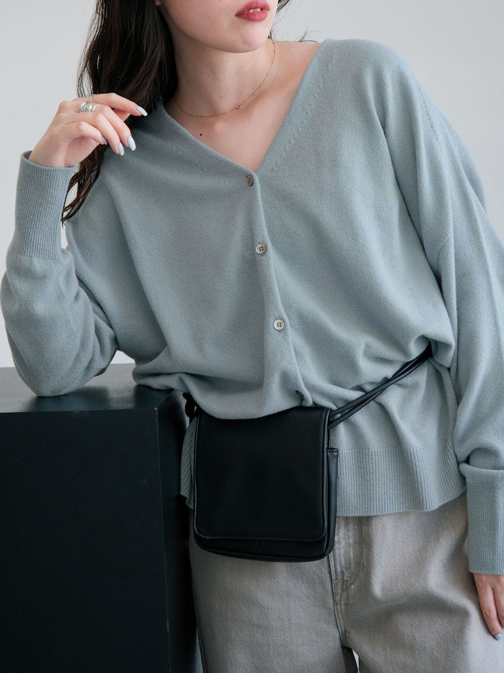 グレー系のデニムパンツ、ブルー系のカーディガン/ボレロ、ブラック系のクラッチバッグを着用したレディースの秋コーディネートの6枚目の写真