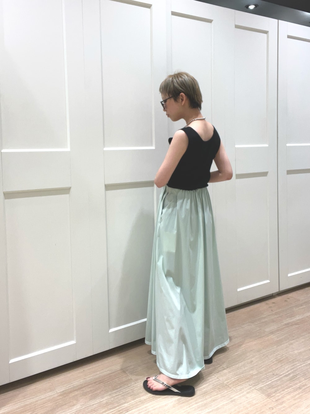 グリーン系のスカート、ブラック系のタンクトップ、ブラック系のショルダーバッグを着用したレディースの夏コーディネートの2枚目の写真