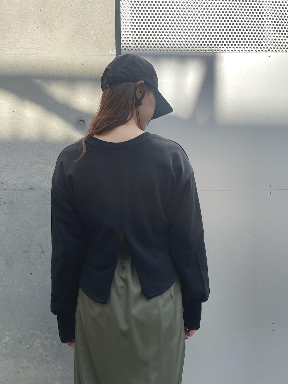 ブラック系のスウェット、グリーン系のスカート、ブラック系のキャップを着用したレディースの春コーディネートの3枚目の写真