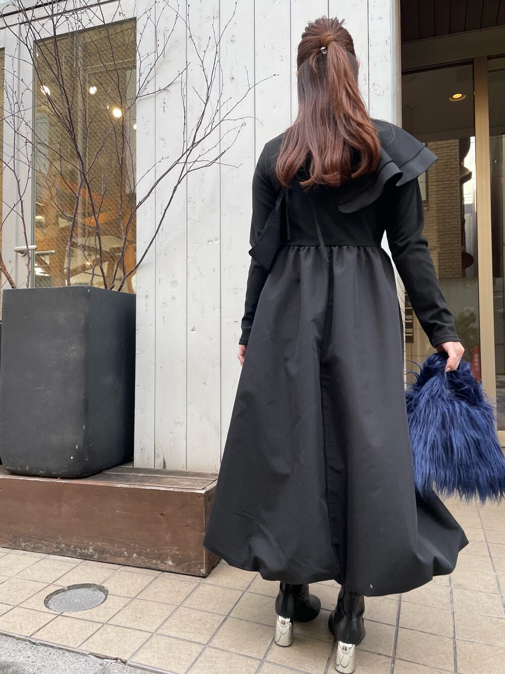 ブルー系のハンドバッグ、ブラック系のワンピース、ゴールド系のピアス（両耳用）を着用したレディースの冬コーディネートの5枚目の写真