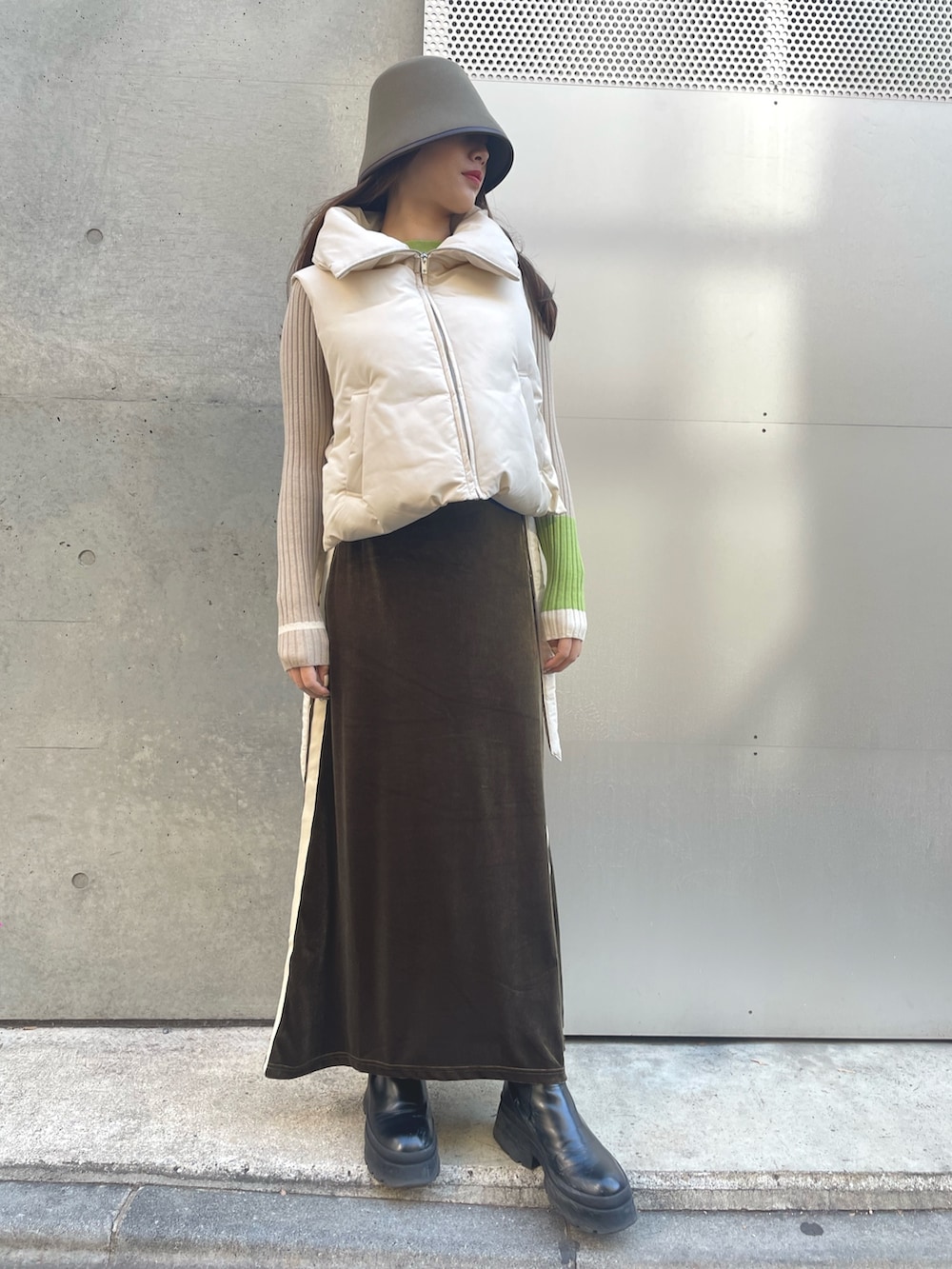 グリーン系のスカート、ベージュ系のニット/セーター、ホワイト系のダウンベストを着用したレディースの冬コーディネートの2枚目の写真