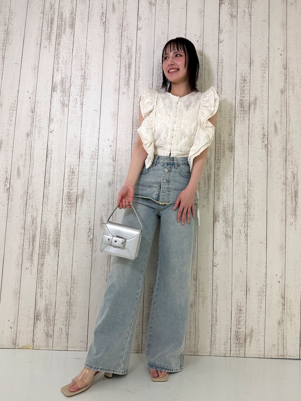 ホワイト系のベスト、ブルー系のデニムパンツ、シルバー系のショルダーバッグを着用したレディースの春コーディネートの2枚目の写真