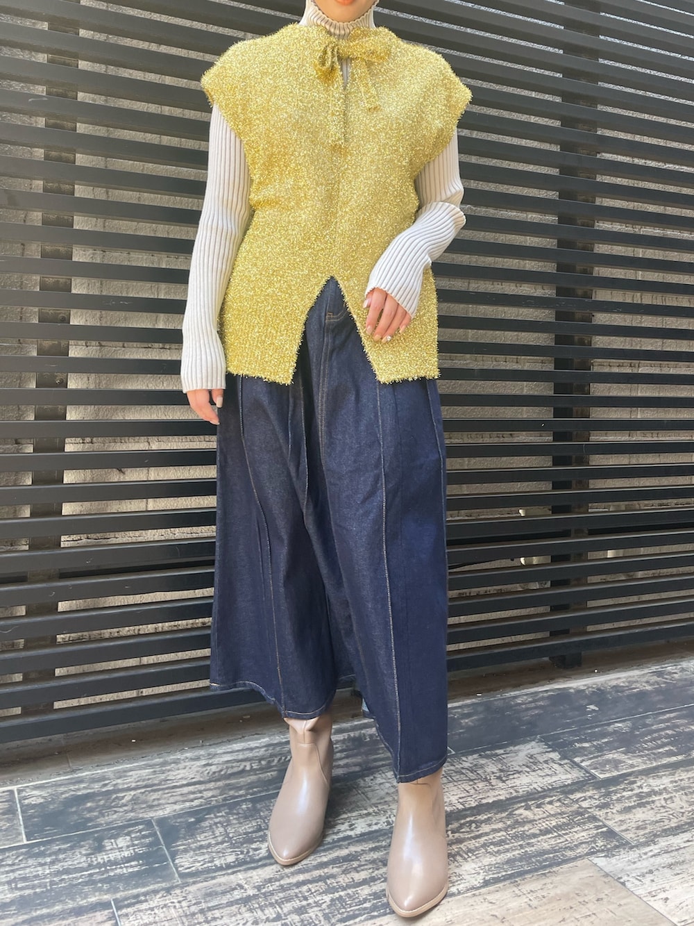 ブルー系のデニムスカート、ホワイト系のニット/セーター、ゴールド系のベストを着用したレディースの冬コーディネートの2枚目の写真