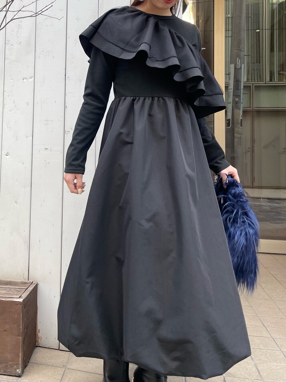 ブルー系のハンドバッグ、ブラック系のワンピース、ゴールド系のピアス（両耳用）を着用したレディースの冬コーディネートの3枚目の写真