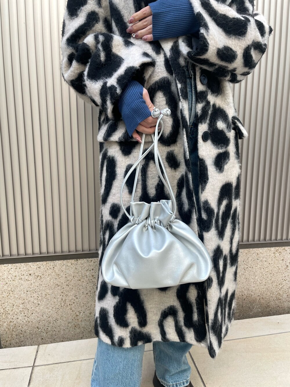 ベージュ系のチェスターコート、ブルー系のニット/セーター、シルバー系のショルダーバッグを着用したレディースの冬コーディネートの4枚目の写真