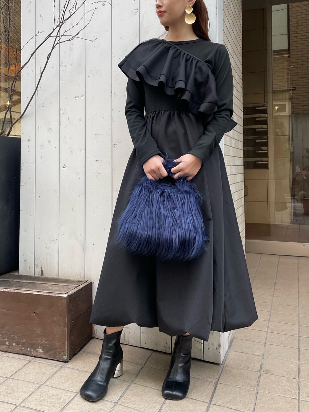 ブルー系のハンドバッグ、ブラック系のワンピース、ゴールド系のピアス（両耳用）を着用したレディースの冬コーディネートの2枚目の写真