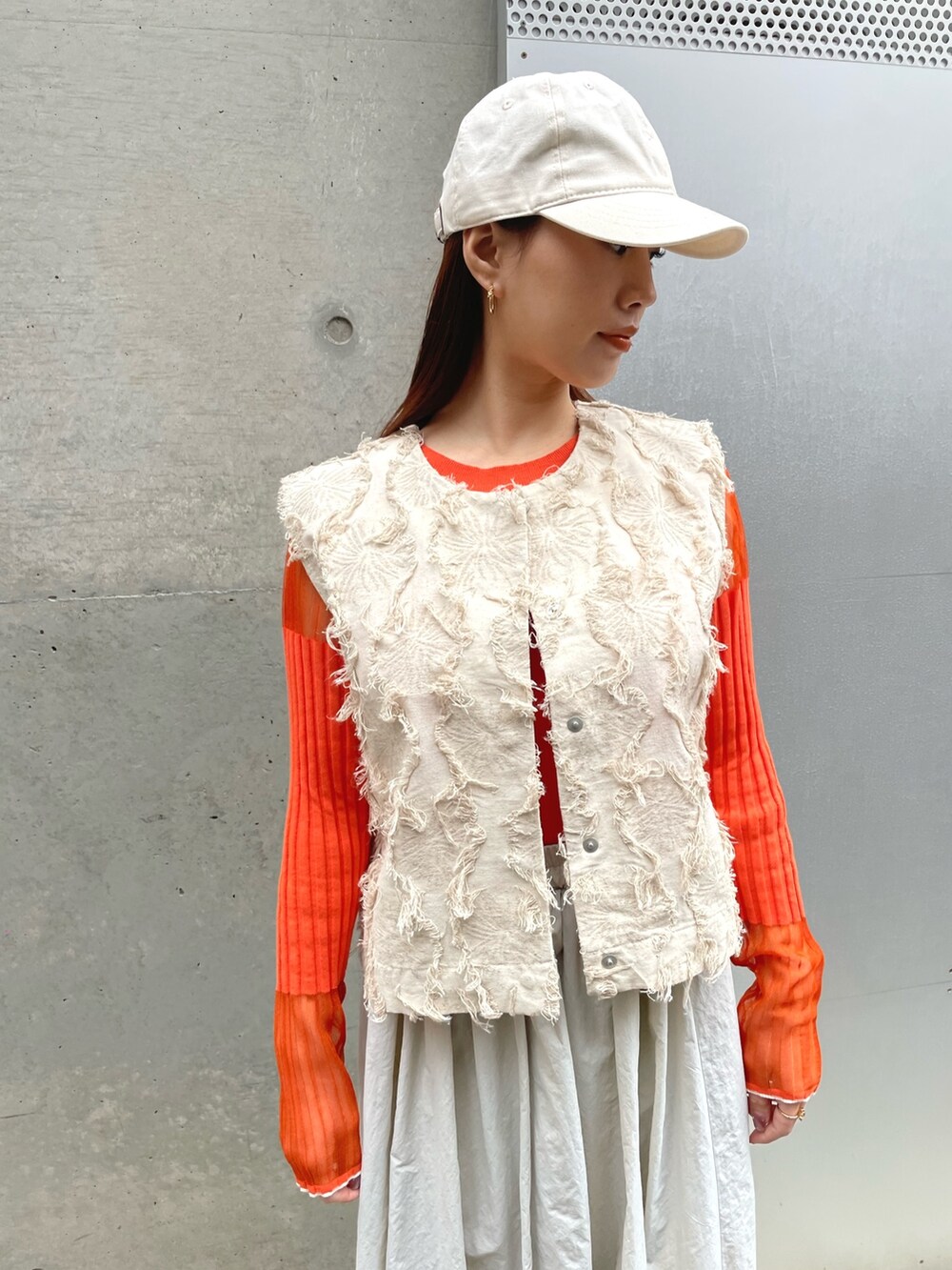 グレー系のスカート、オレンジ系のニット/セーター、ホワイト系のベストを着用したレディースの冬コーディネートの2枚目の写真