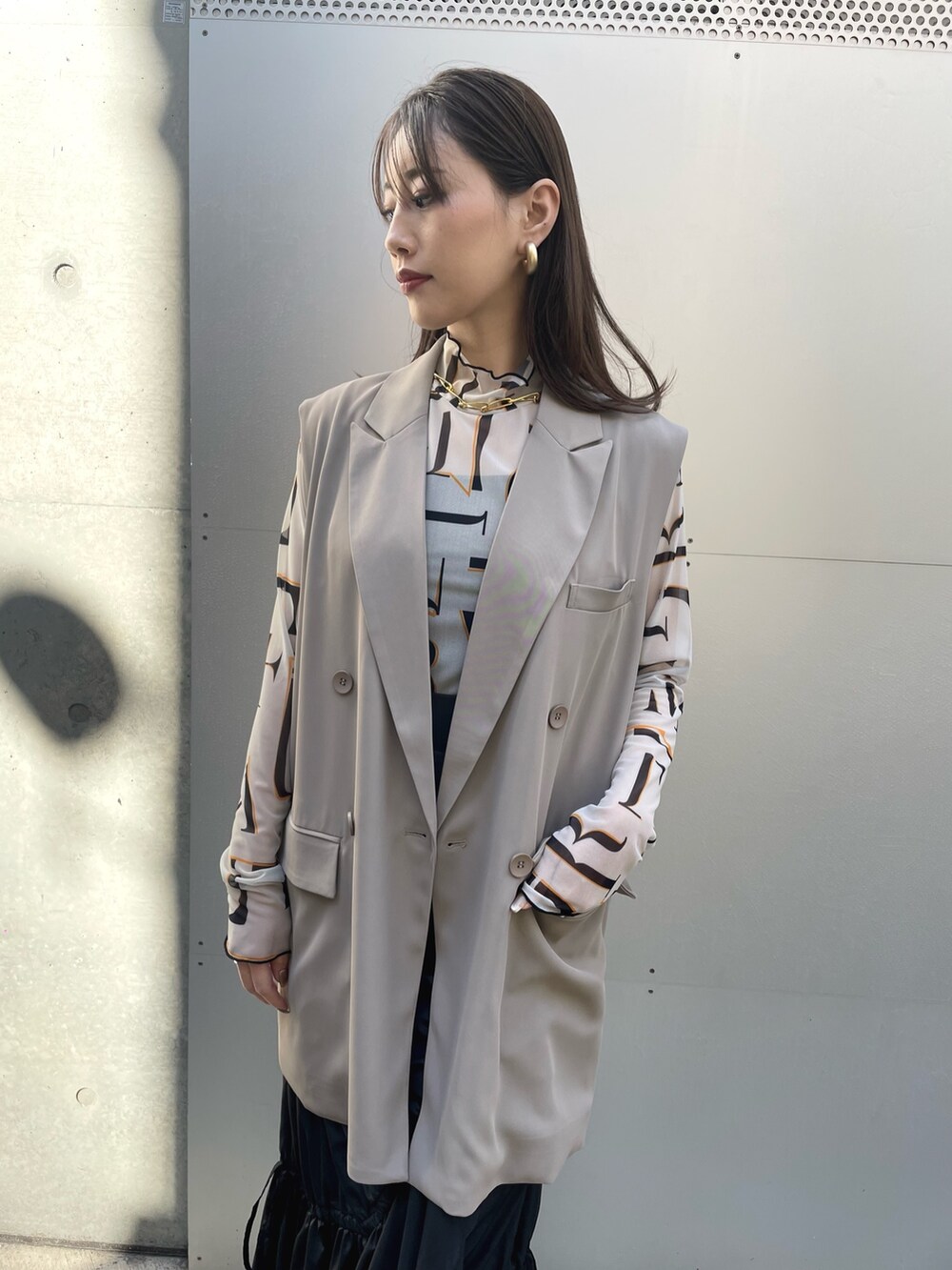 ブラック系のスカート、グレー系のベスト、ベージュ系のトップスを着用したレディースの春コーディネートの2枚目の写真