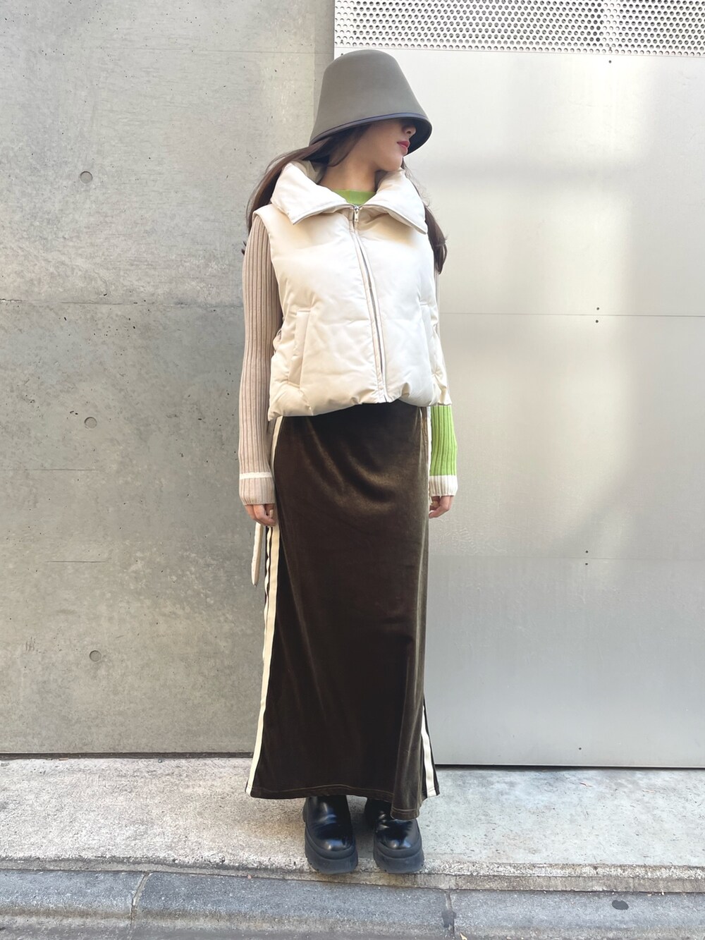 グリーン系のスカート、ベージュ系のニット/セーター、ホワイト系のダウンベストを着用したレディースの冬コーディネートの3枚目の写真