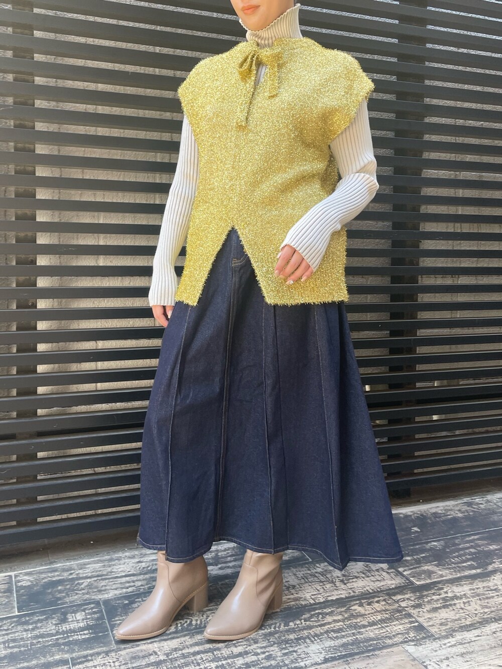 ブルー系のデニムスカート、ホワイト系のニット/セーター、ゴールド系のベストを着用したレディースの冬コーディネートの3枚目の写真