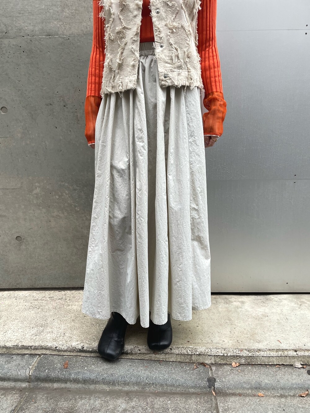 グレー系のスカート、オレンジ系のニット/セーター、ホワイト系のベストを着用したレディースの冬コーディネートの3枚目の写真