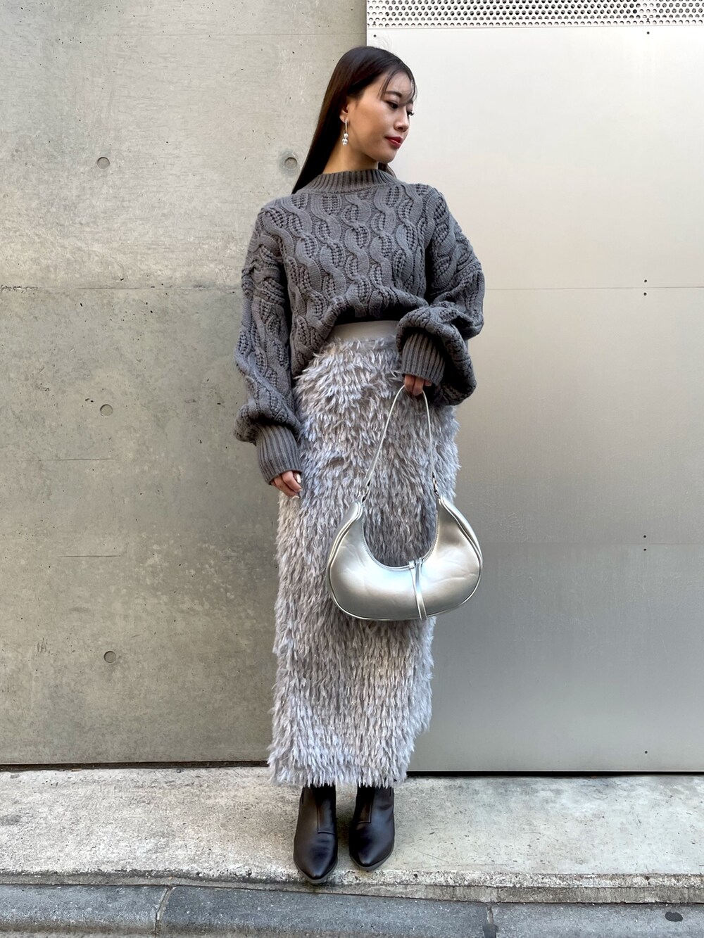 グレー系のニット/セーター、シルバー系のショルダーバッグ、グレー系のスカートを着用したレディースの冬コーディネートの3枚目の写真