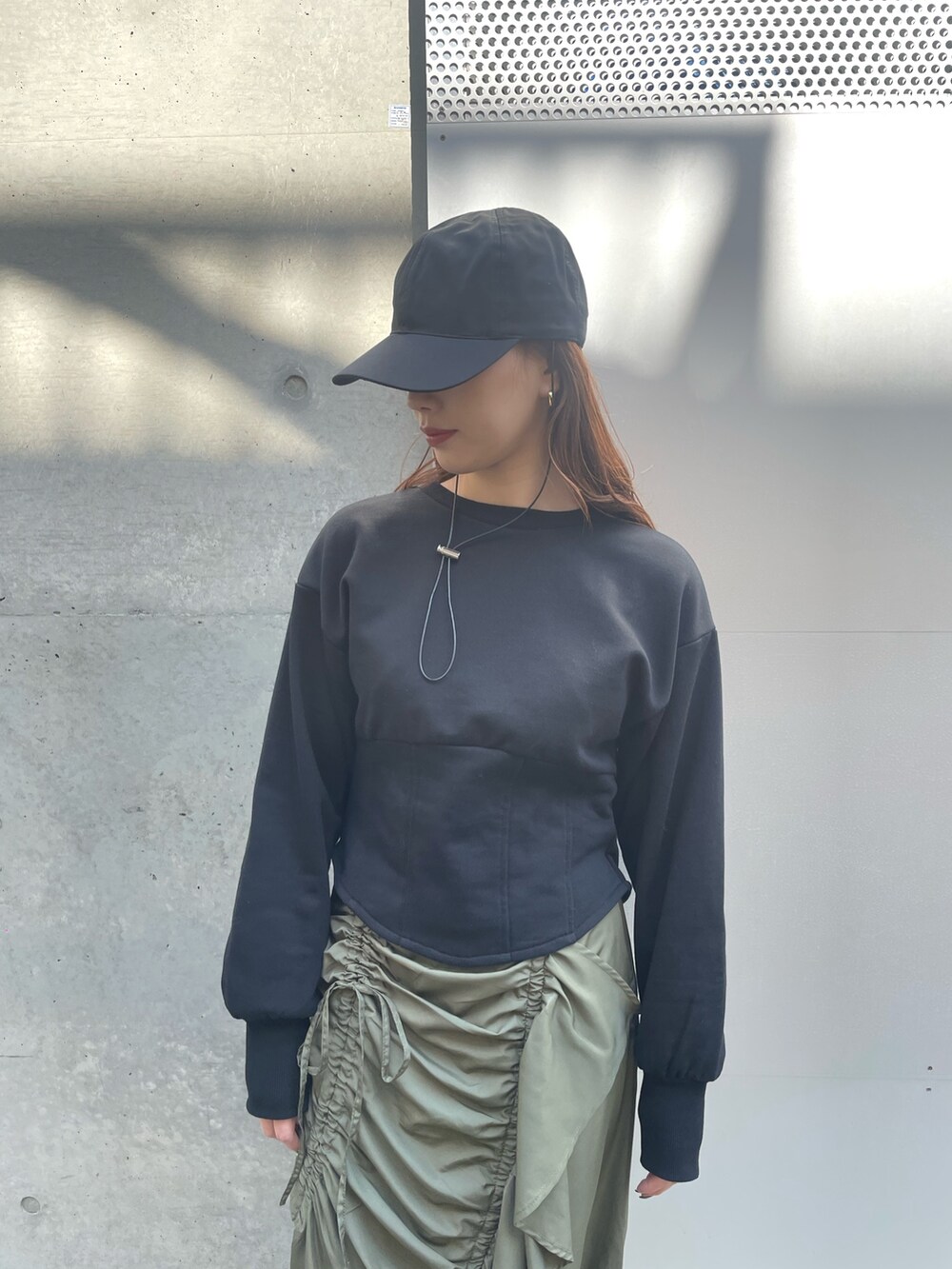 ブラック系のスウェット、グリーン系のスカート、ブラック系のキャップを着用したレディースの春コーディネートの2枚目の写真