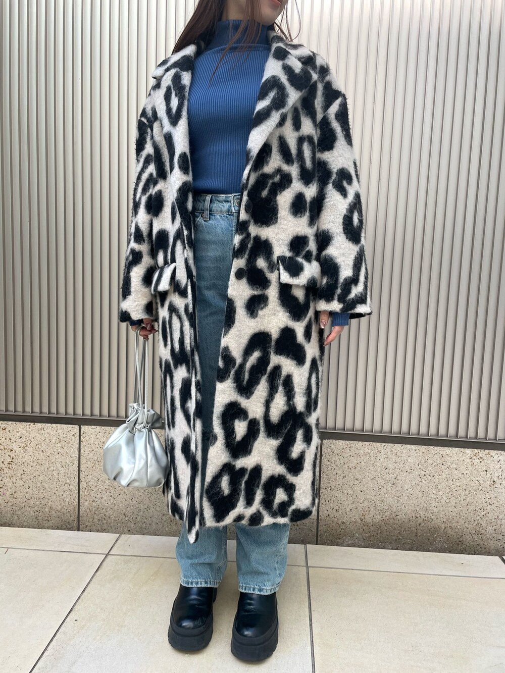 ベージュ系のチェスターコート、ブルー系のニット/セーター、シルバー系のショルダーバッグを着用したレディースの冬コーディネートの3枚目の写真