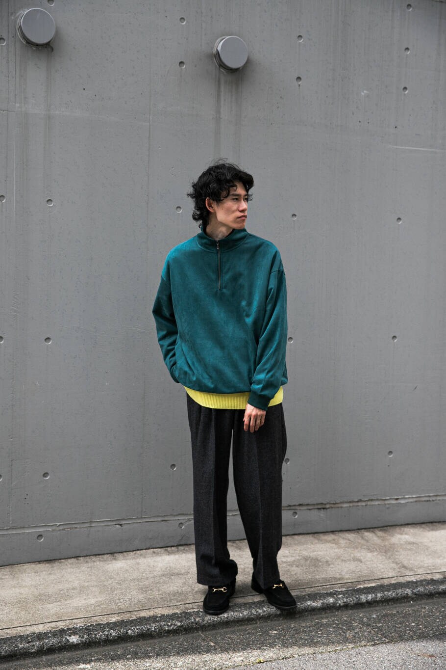 イエロー系のニット/セーター、グリーン系のTシャツ/カットソー、グレー系のスラックスを着用したメンズの冬コーディネートの2枚目の写真