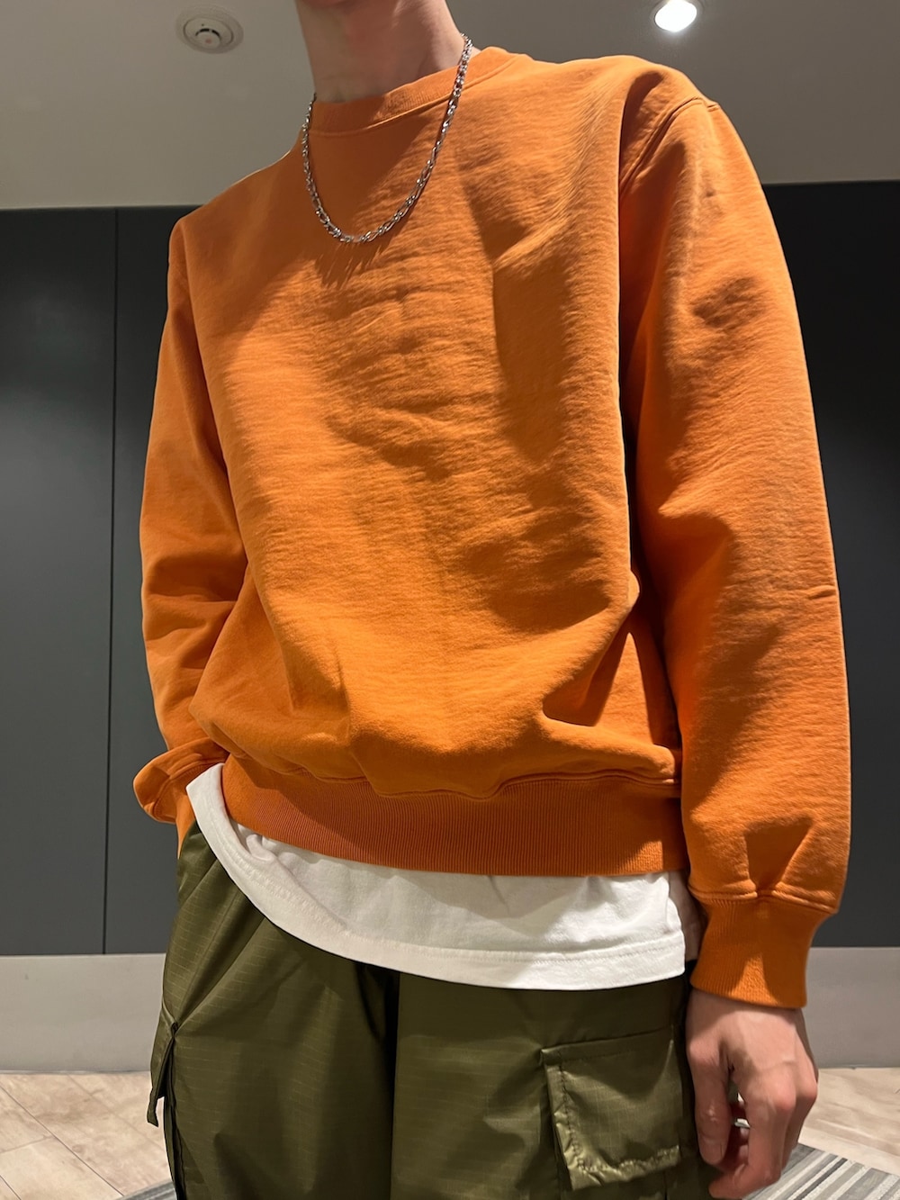 オレンジ系のスウェット、ブラウン系のモカシン/デッキシューズ、シルバー系のネックレスを着用したメンズの春コーディネートの2枚目の写真