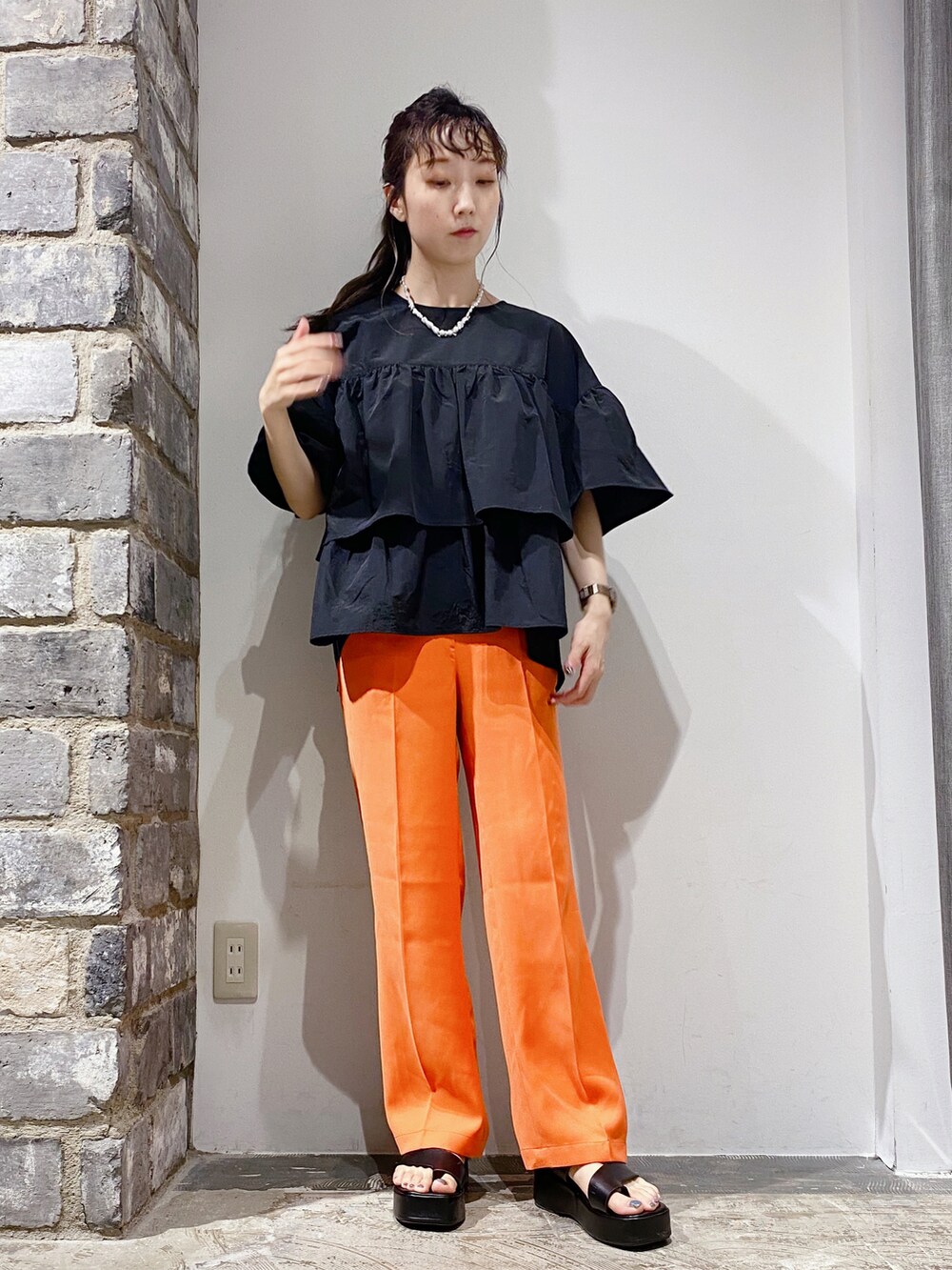 ブラック系のシャツ/ブラウス、オレンジ系のスラックス、ブラック系のサンダルを着用したレディースの夏コーディネートの2枚目の写真