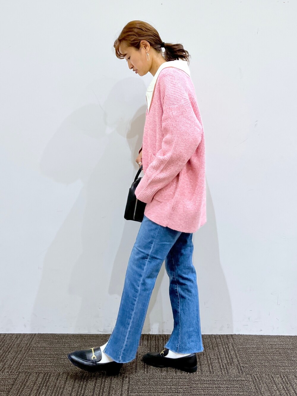 ブラック系のショルダーバッグ、ブルー系のデニムパンツ、ピンク系のカーディガン/ボレロを着用したレディースの秋コーディネートの2枚目の写真