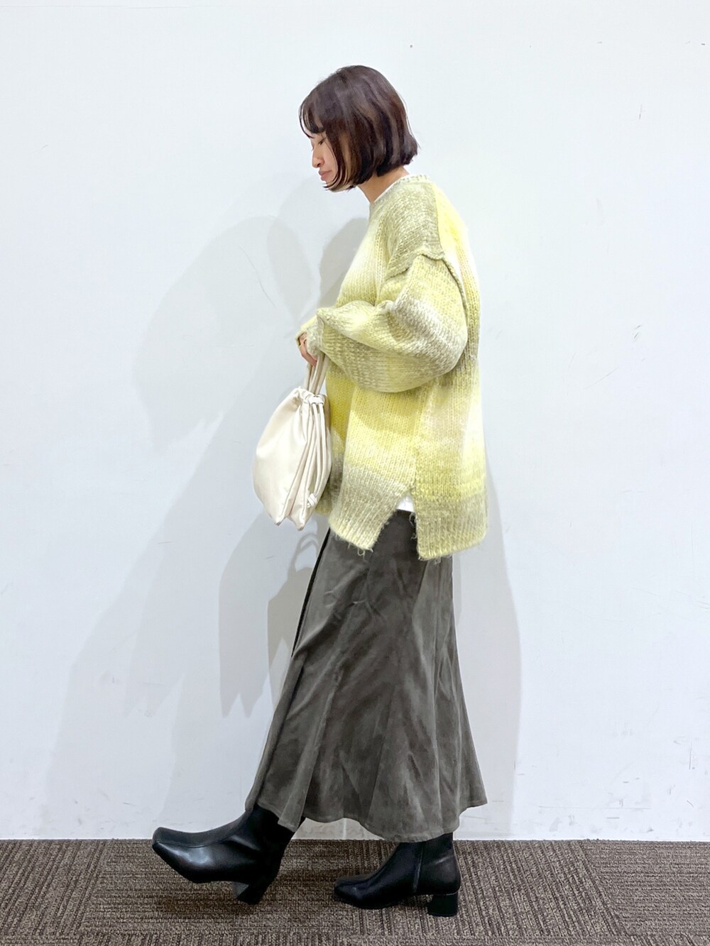 ブラック系のブーツ、ホワイト系のバッグ、グレー系のスカートを着用したレディースの秋コーディネートの2枚目の写真