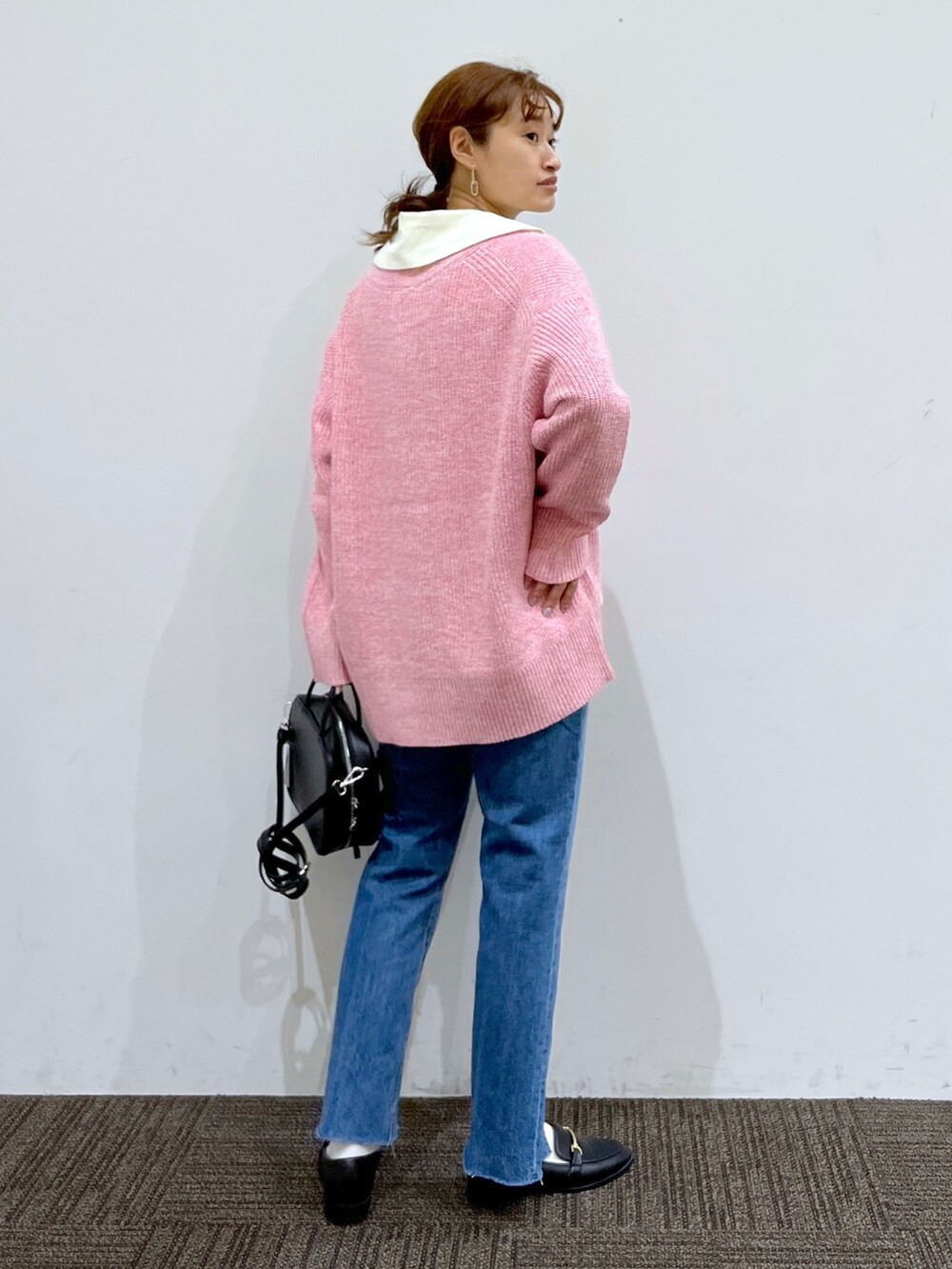 ブラック系のショルダーバッグ、ブルー系のデニムパンツ、ピンク系のカーディガン/ボレロを着用したレディースの秋コーディネートの3枚目の写真