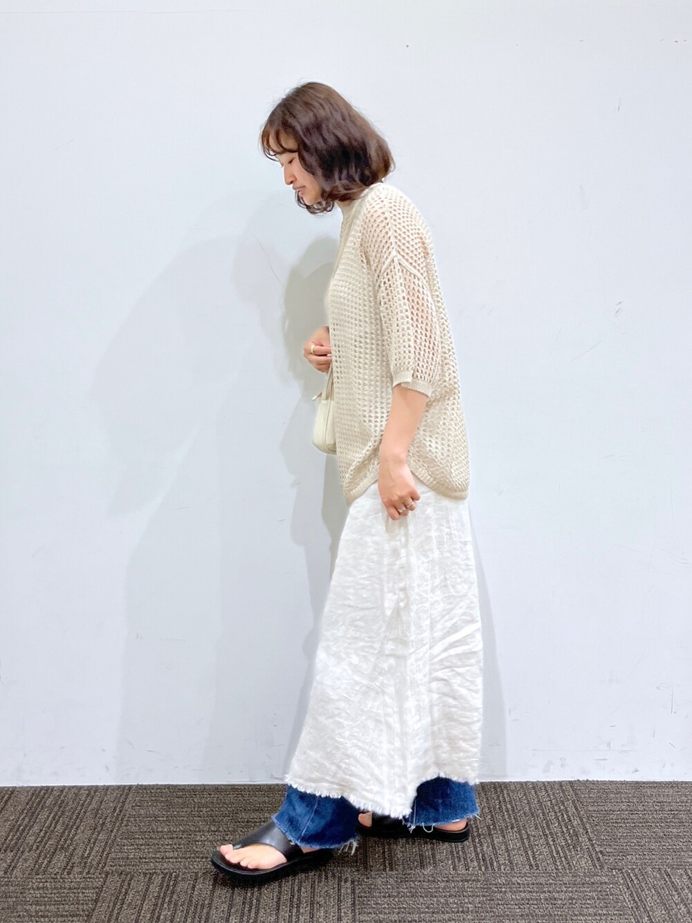 ブルー系のデニムパンツ、ホワイト系のスカート、ホワイト系のショルダーバッグを着用したレディースの春コーディネートの2枚目の写真