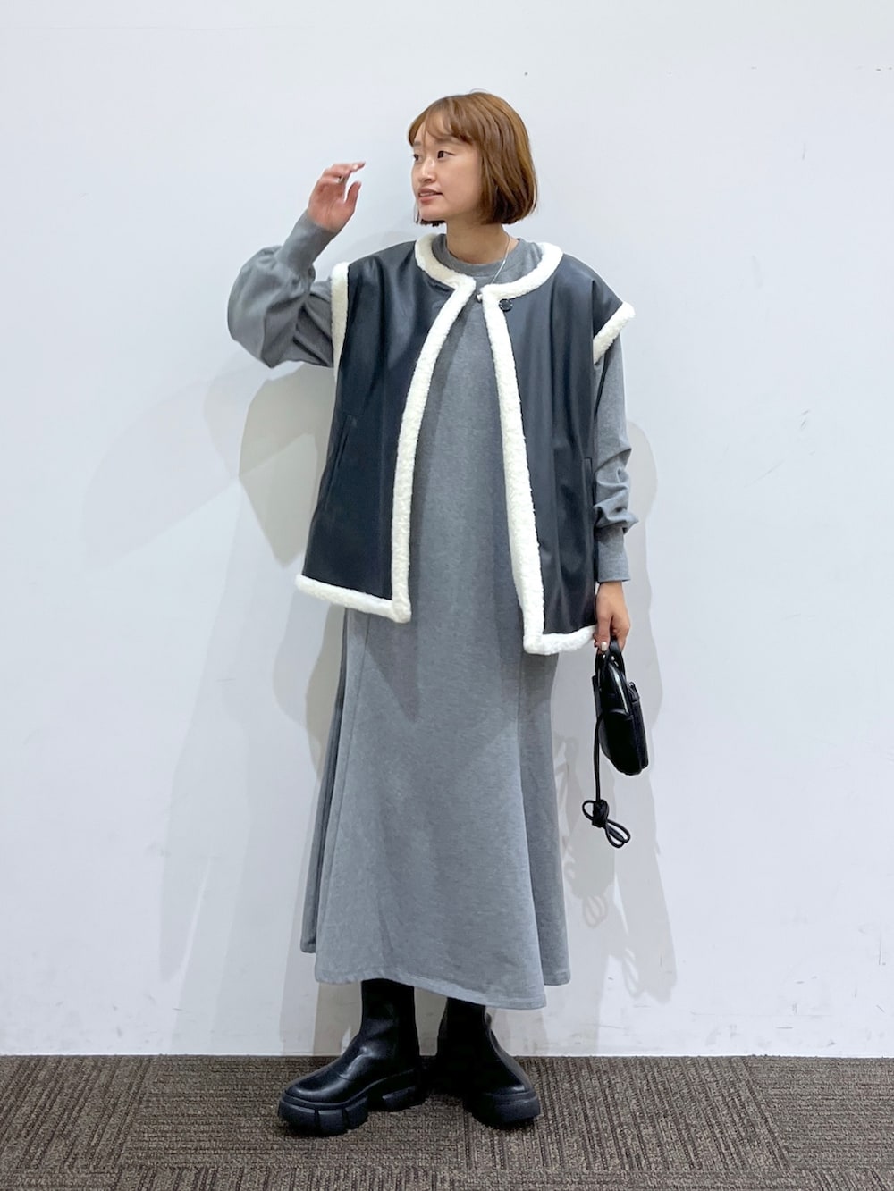 グレー系のワンピース、ブラック系のショルダーバッグ、ブラック系のブーツを着用したレディースの秋コーディネートの2枚目の写真