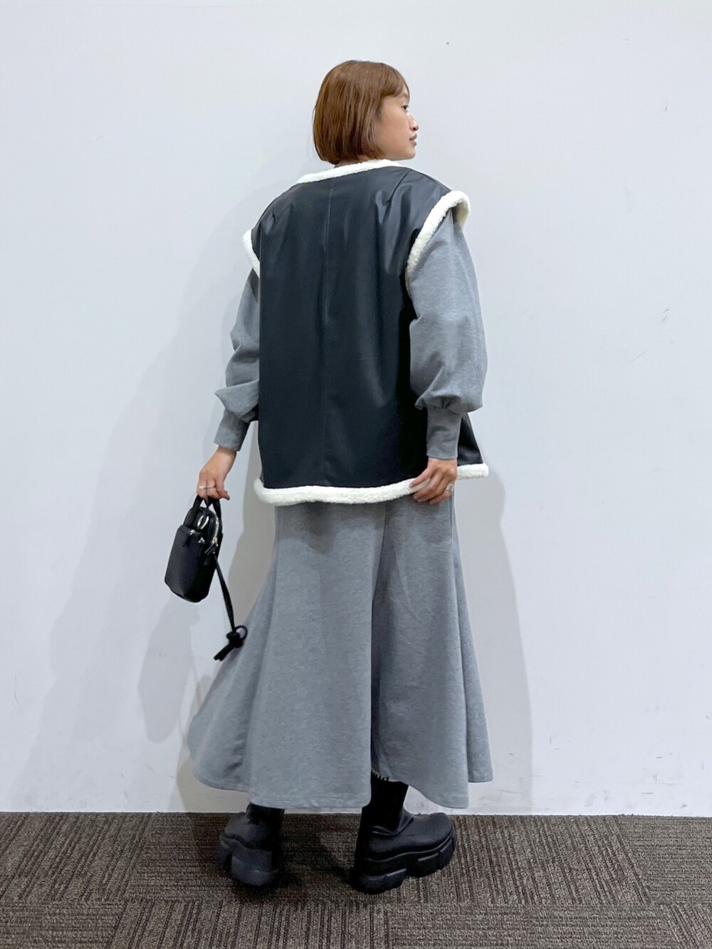 グレー系のワンピース、ブラック系のショルダーバッグ、ブラック系のブーツを着用したレディースの秋コーディネートの3枚目の写真