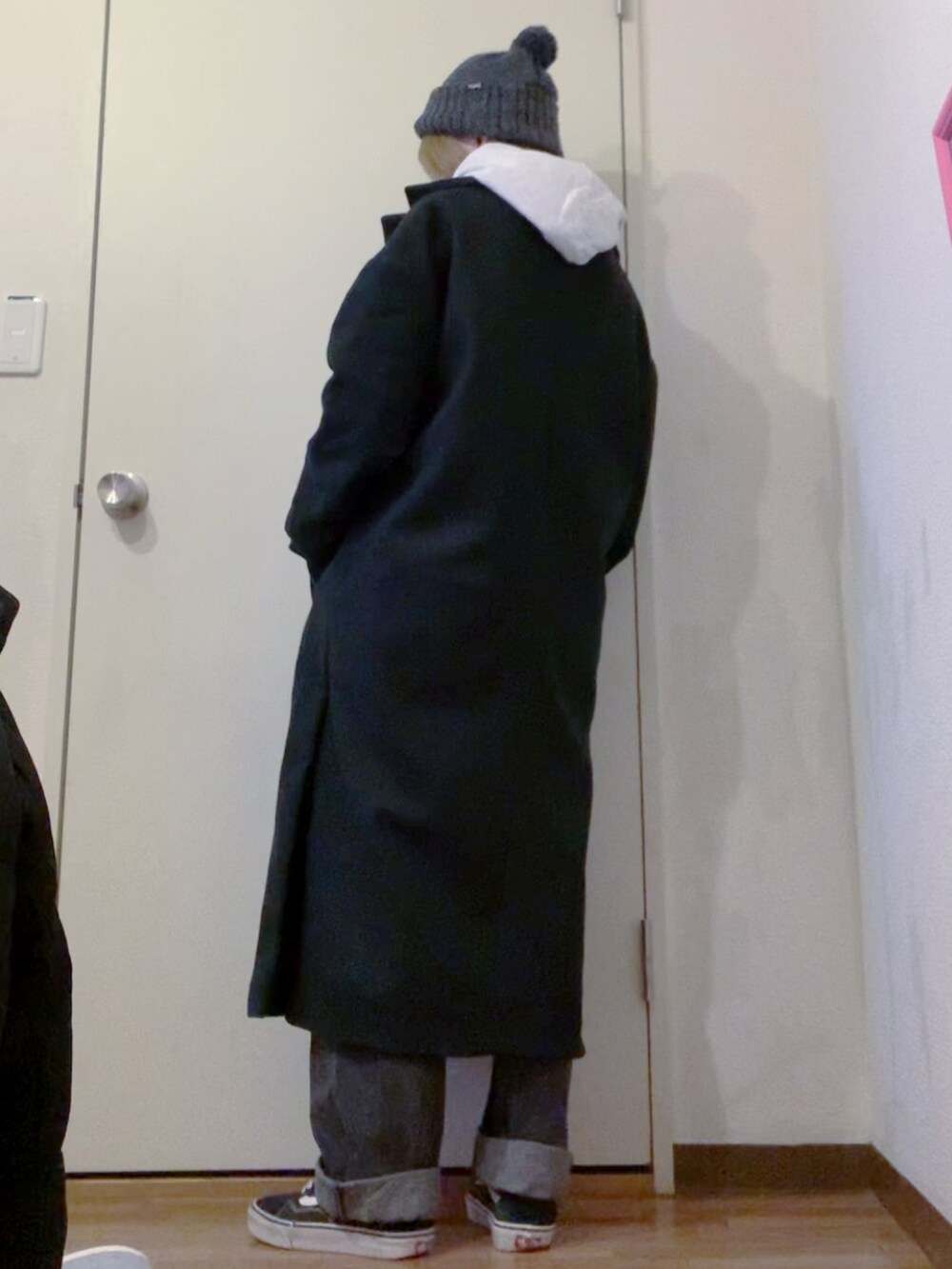グレー系のパーカー、ブラック系のデニムパンツ、ブラック系のチェスターコートを着用したレディースの冬コーディネートの2枚目の写真