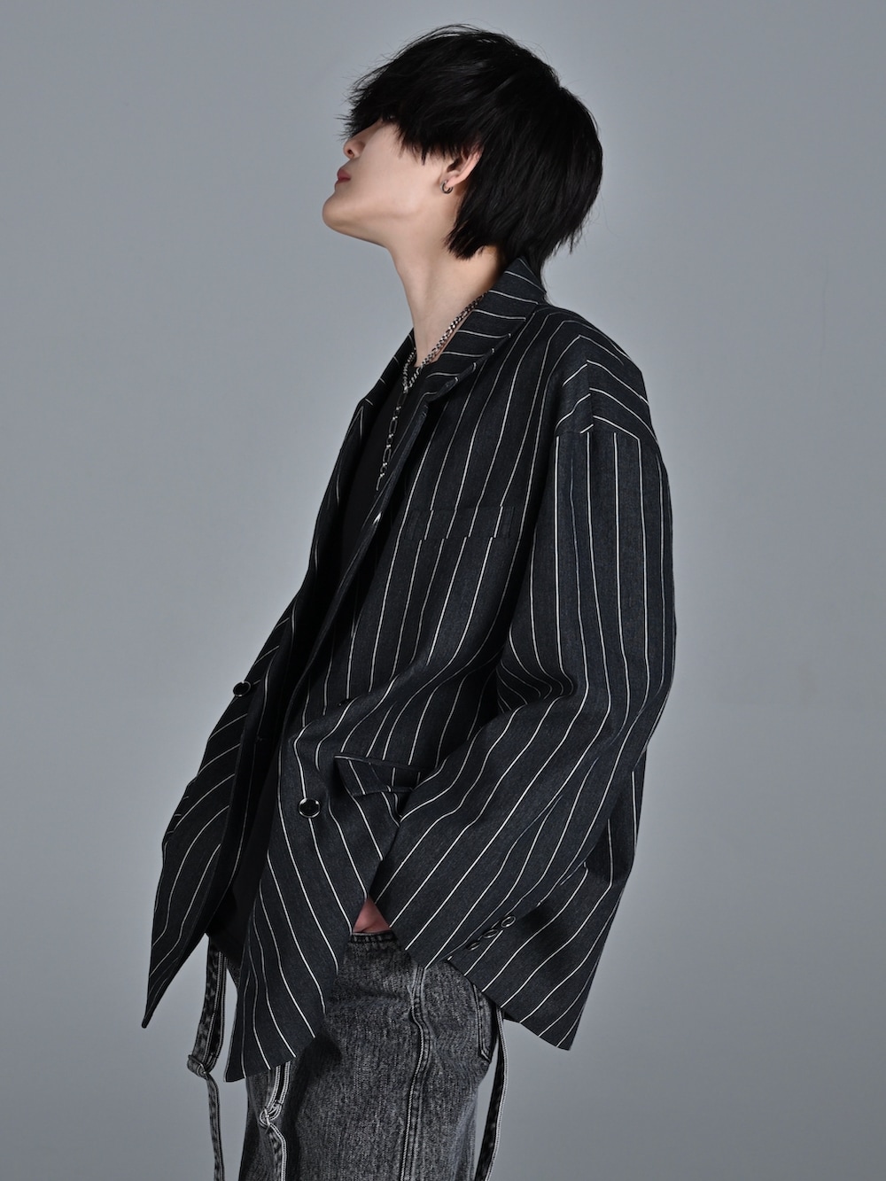 レッド系のタンクトップ、ブラック系のテーラードジャケット、ブラック系のデニムパンツを着用したメンズの冬コーディネートの3枚目の写真