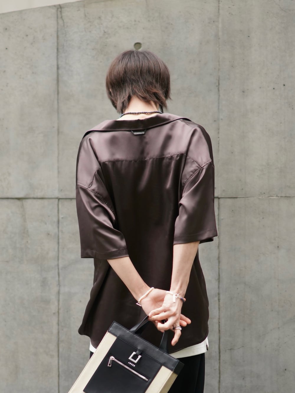 ブラック系のスラックス、ブラック系のブーツ、ベージュ系のトートバッグを着用したメンズの春コーディネートの3枚目の写真