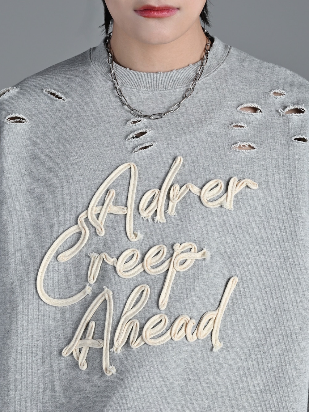 グレー系のスウェット、ブルー系のデニムパンツ、シルバー系のネックレスを着用したメンズの冬コーディネートの4枚目の写真