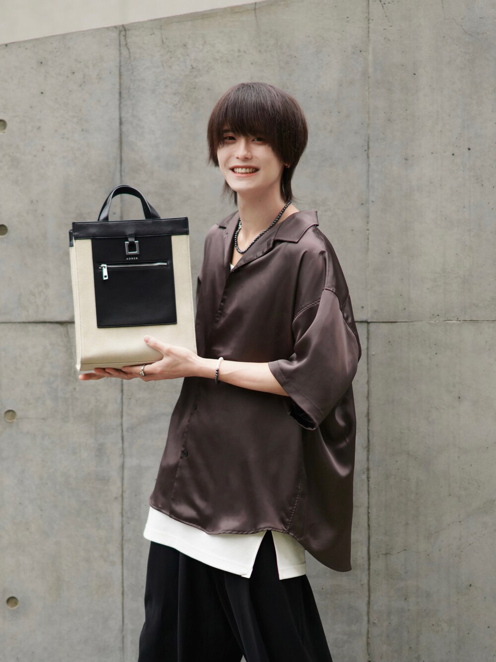 ブラック系のスラックス、ブラック系のブーツ、ベージュ系のトートバッグを着用したメンズの春コーディネートの2枚目の写真