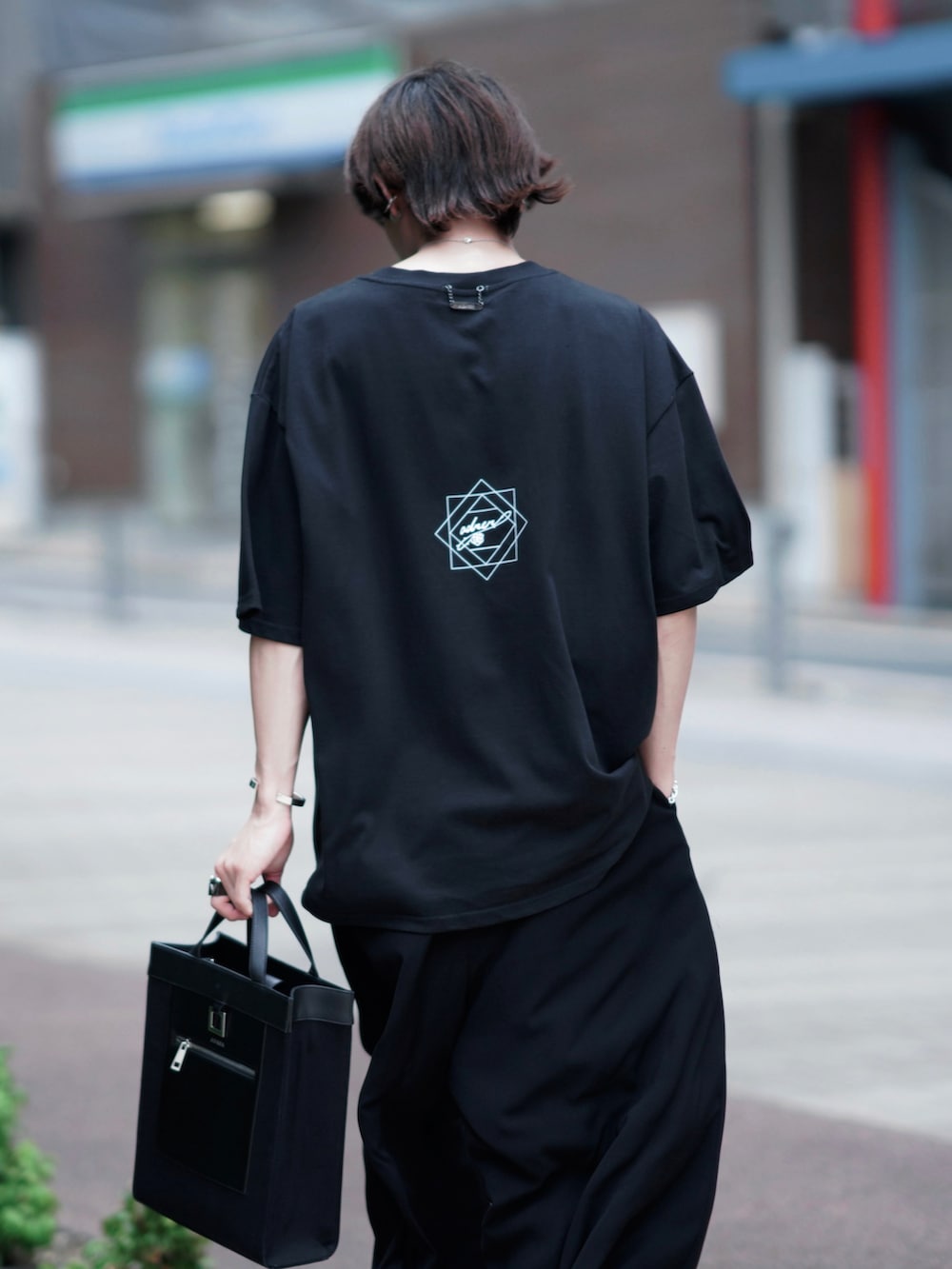 ブラック系のトートバッグ、ブラック系のスラックス、ブラック系のブーツを着用したメンズの夏コーディネートの4枚目の写真