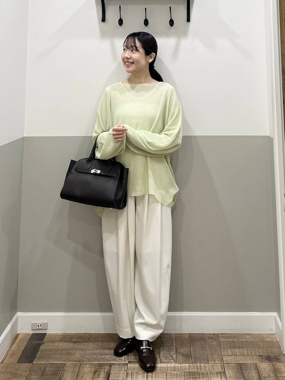 ホワイト系のスラックス、ブラウン系のショルダーバッグ、グリーン系のニット/セーターを着用したレディースの春コーディネートの3枚目の写真