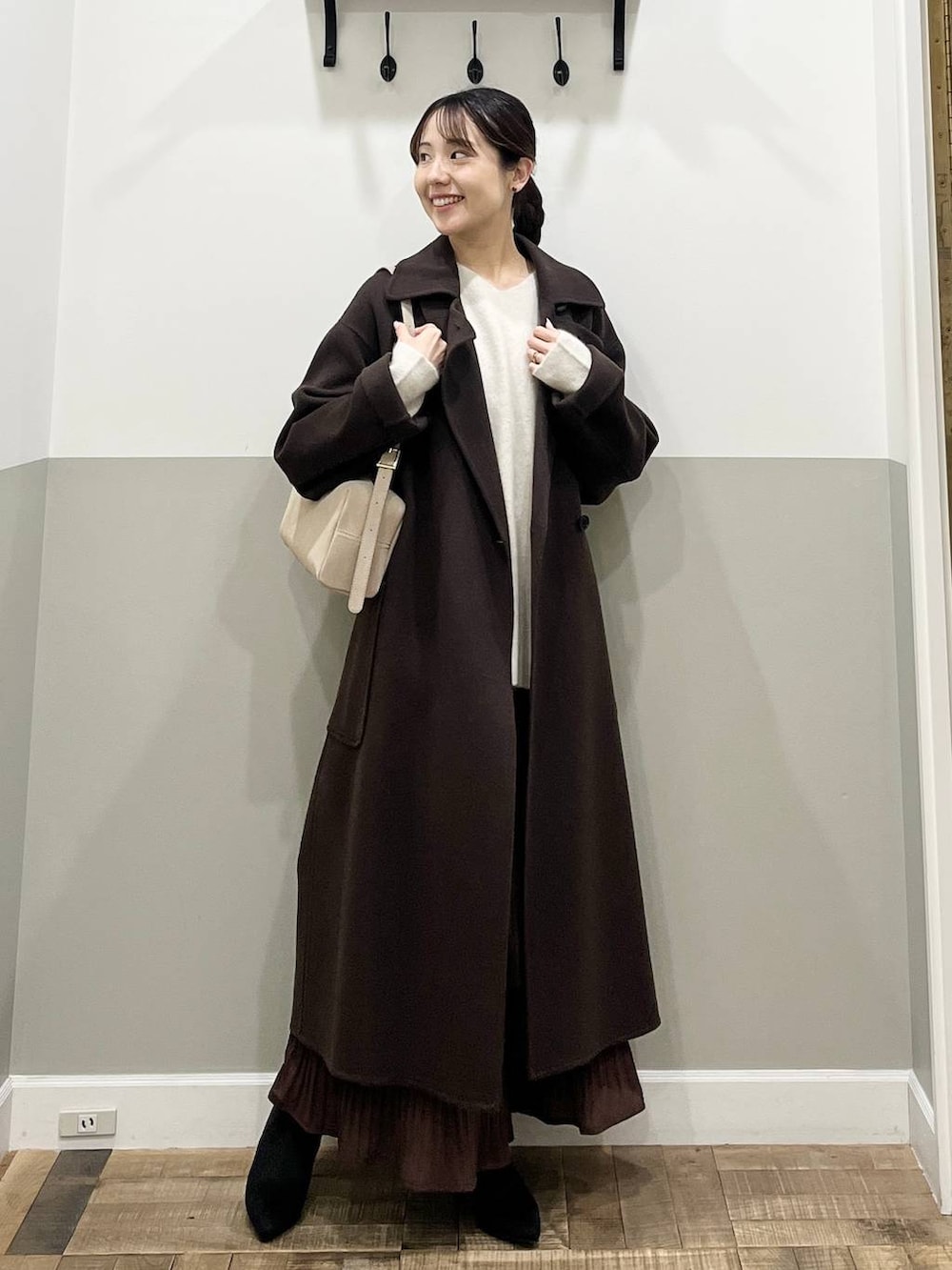 ブラウン系のステンカラーコート、ホワイト系のニット/セーター、ブラウン系のスカートを着用したレディースの秋コーディネートの2枚目の写真