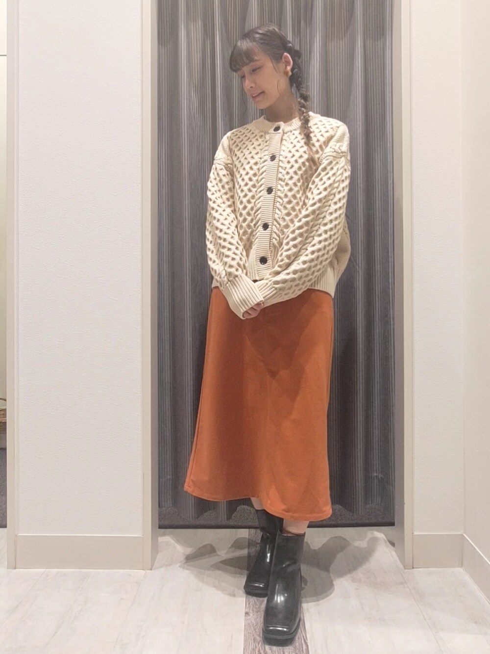 ホワイト系のカーディガン/ボレロ、オレンジ系のスカート、ブラック系のブーツを着用したレディースの秋コーディネートの2枚目の写真