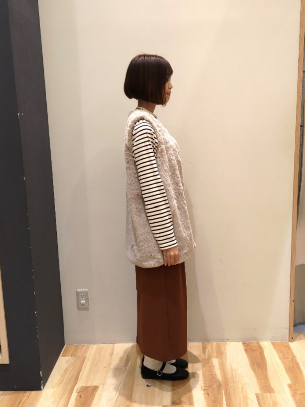 ベージュ系のベスト、オレンジ系のスカート、ブラック系のドレスシューズを着用したレディースの秋コーディネートの2枚目の写真