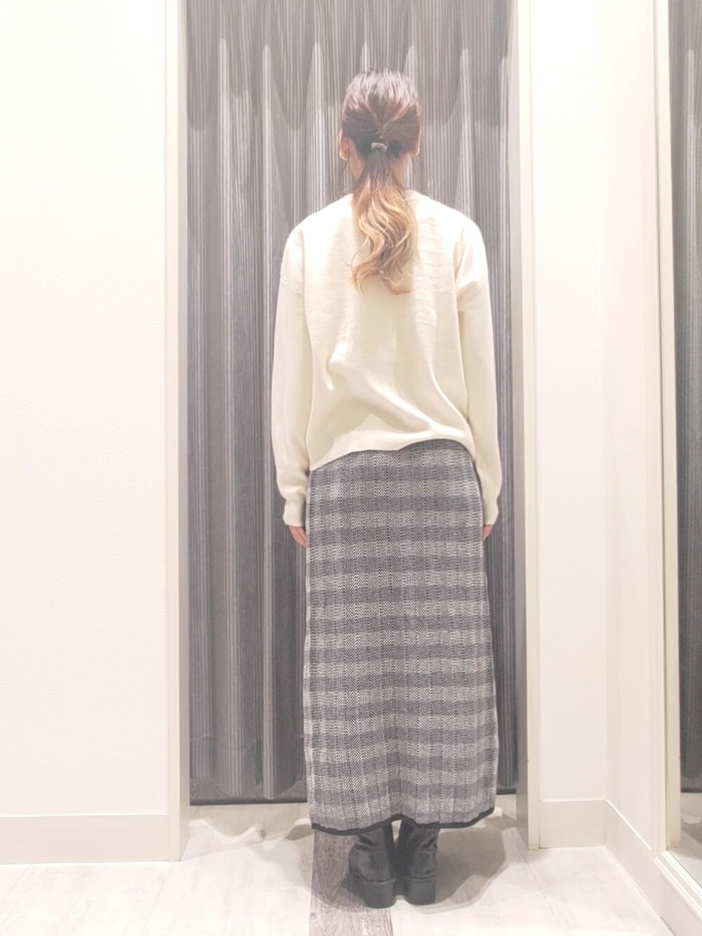 ホワイト系のハンドバッグ、ブラック系のスカート、ブラック系のブーツを着用したレディースの秋コーディネートの3枚目の写真