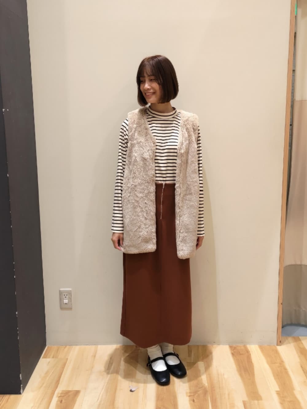 ベージュ系のベスト、オレンジ系のスカート、ブラック系のドレスシューズを着用したレディースの秋コーディネートの4枚目の写真