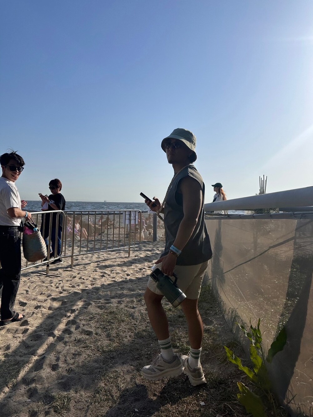 グレー系のタンクトップ、ホワイト系のその他パンツ、グリーン系のハットを着用したメンズの夏コーディネートの2枚目の写真