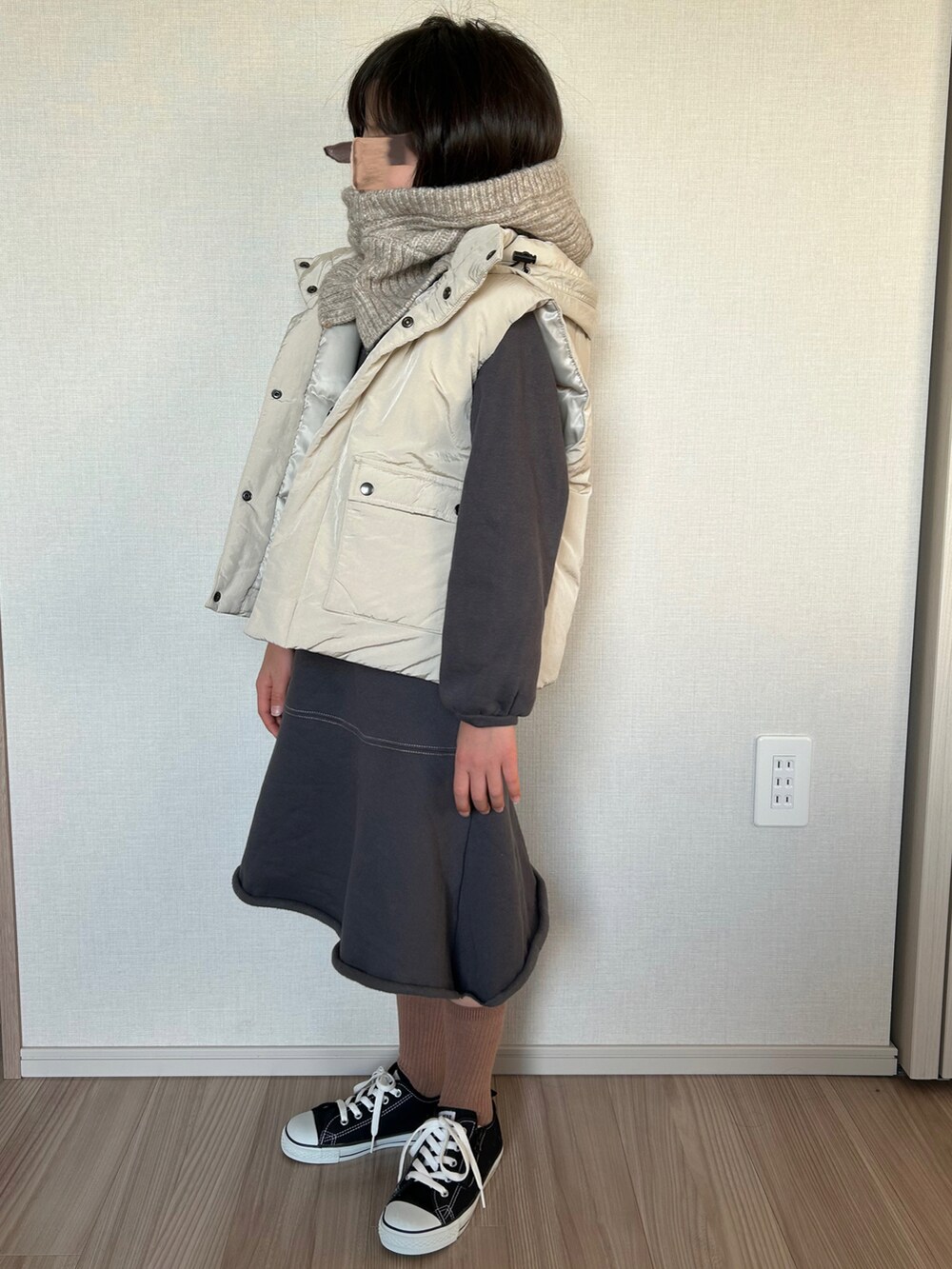 ホワイト系のダウンベスト、グレー系のワンピース、ブラック系のスニーカーを着用したキッズの冬コーディネートの2枚目の写真