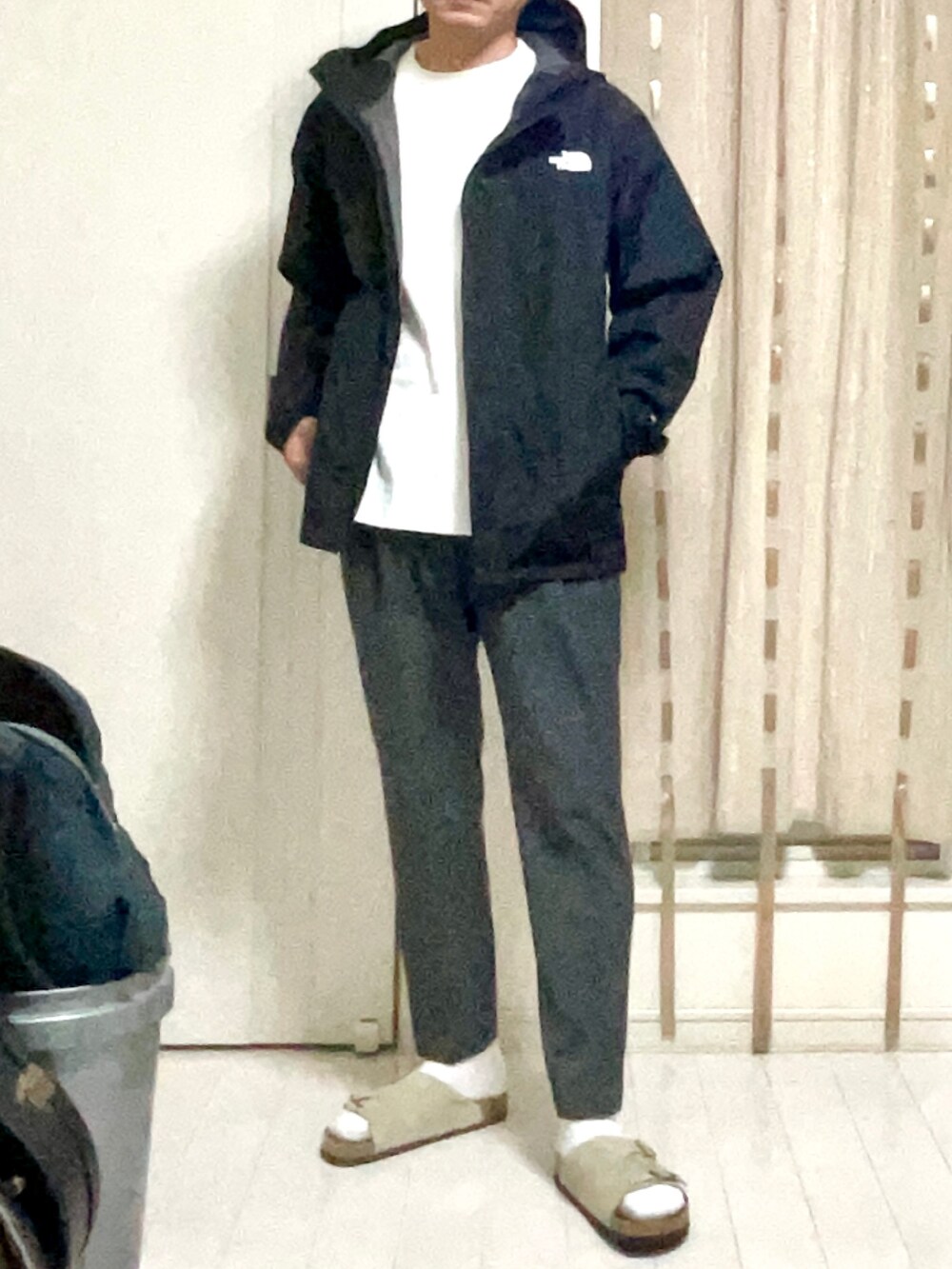 ブラック系のマウンテンパーカー、ホワイト系のTシャツ/カットソー、グレー系のスラックスを着用したメンズの春コーディネートの2枚目の写真