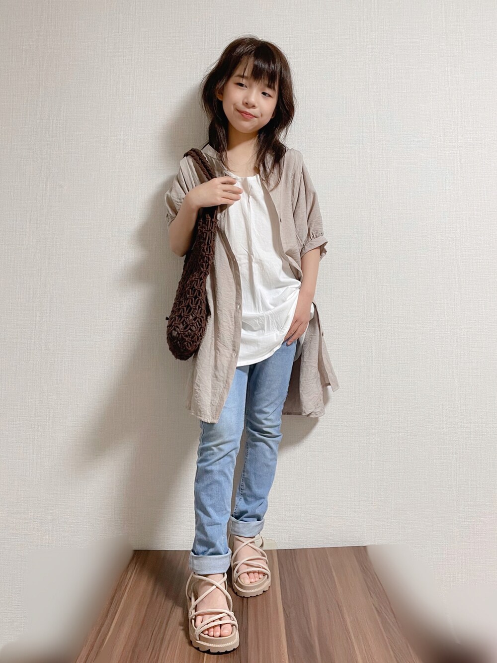 ベージュ系のワンピース、ホワイト系のタンクトップ、ブルー系のデニムパンツを着用したキッズの春コーディネートの2枚目の写真