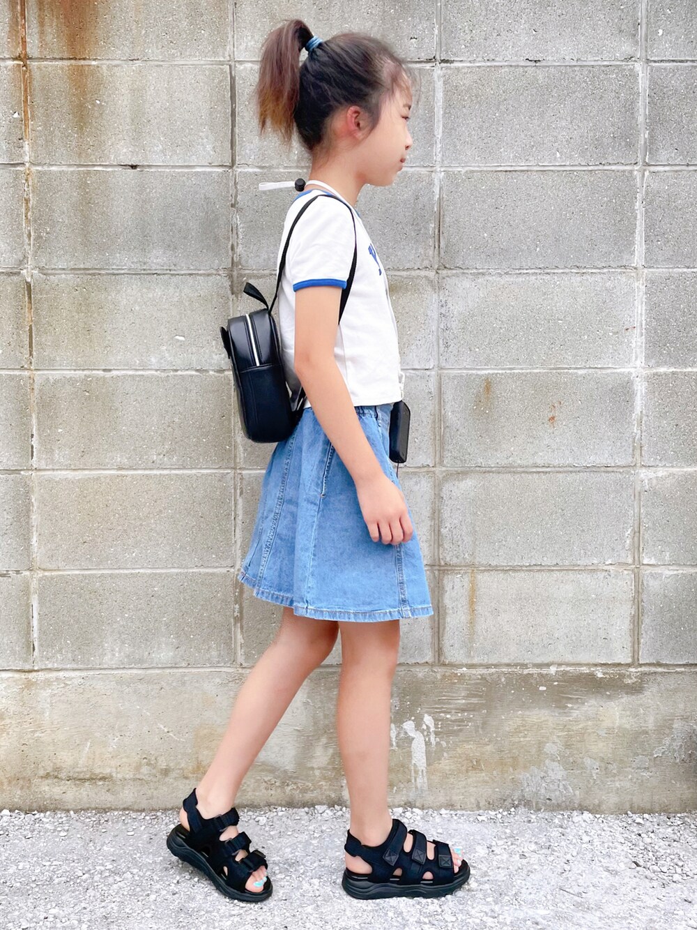 ブラック系のサンダル、ホワイト系のTシャツ/カットソー、ブルー系のデニムスカートを着用したキッズの夏コーディネートの2枚目の写真