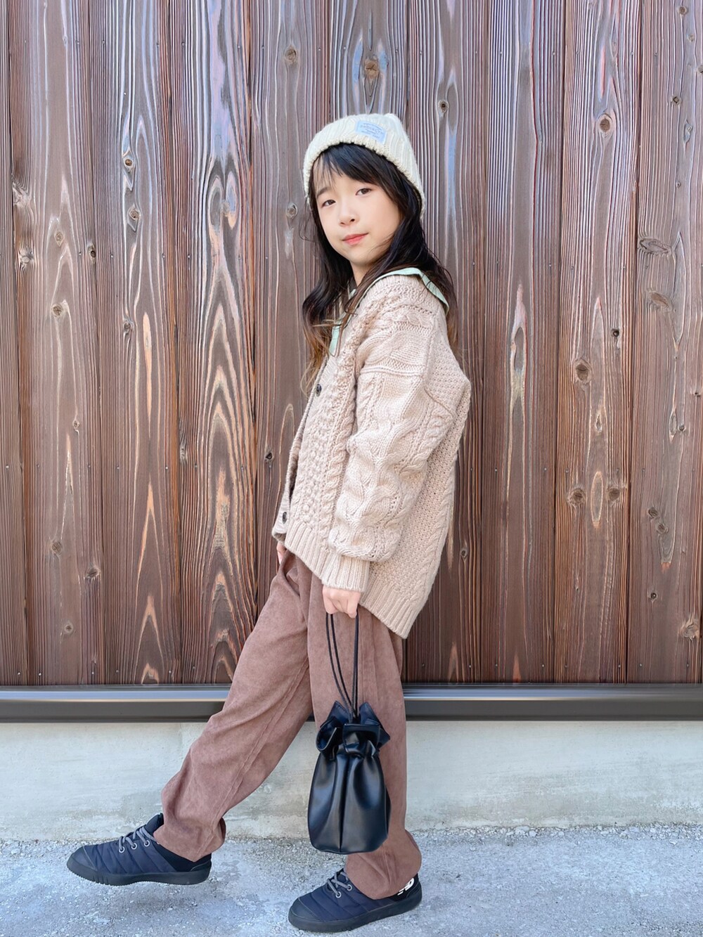 ブラック系のハンドバッグ、ブラック系のスニーカー、ベージュ系のカーディガン/ボレロを着用したキッズの秋コーディネートの2枚目の写真